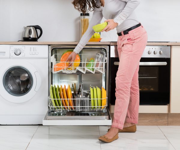 Woman Standing In Kitchen Removing Bowls From Dishwasher